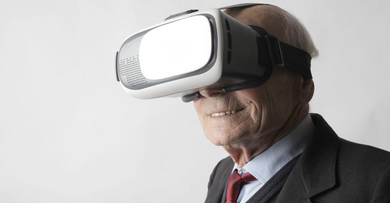 Wearable Devices - Smiling elderly gentleman wearing classy suit experiencing virtual reality while using modern headset on white background