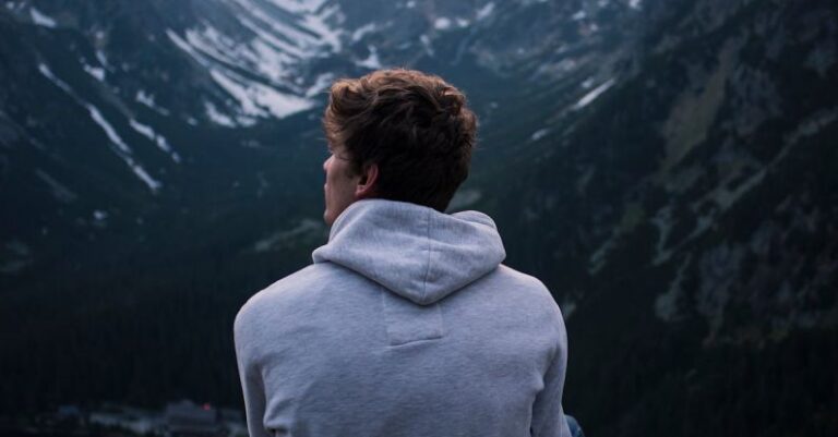 Solo Travelers - A Man in White Hoodie Sitting on a Rock Across the Mountains