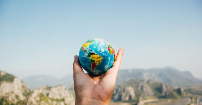 Travel Insurance - Person Holding World Globe Facing Mountain