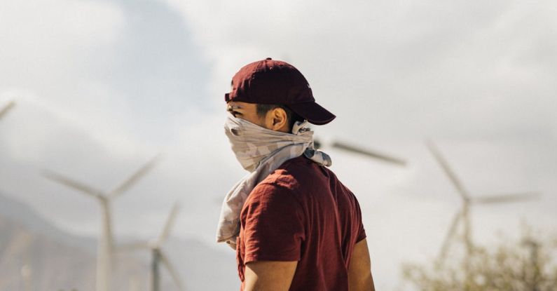 Sustainable Travel - Unrecognizable man with scarf on face walking in sandy terrain terrain near windmills