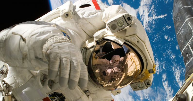 Space Discoveries - This picture shows an american astronaut in his space and extravehicular activity suite working outside of a spacecraft. In the background parts of a space shuttle are visible. In the far background of the picture planet earth with it's blue color and white clouds is shown as well as a patch of black space.