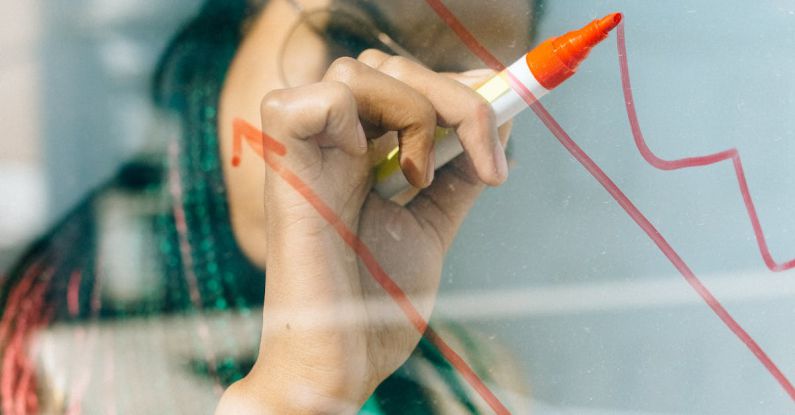 Investment Strategies - Woman in a Beige Coat Writing on a Glass Panel Using a Whiteboard Marker